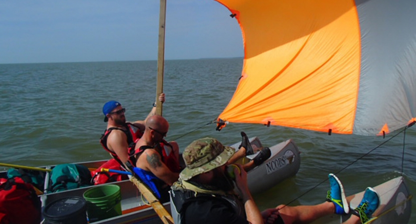 three people sit in canoes using a tarp as a makeshift sail.